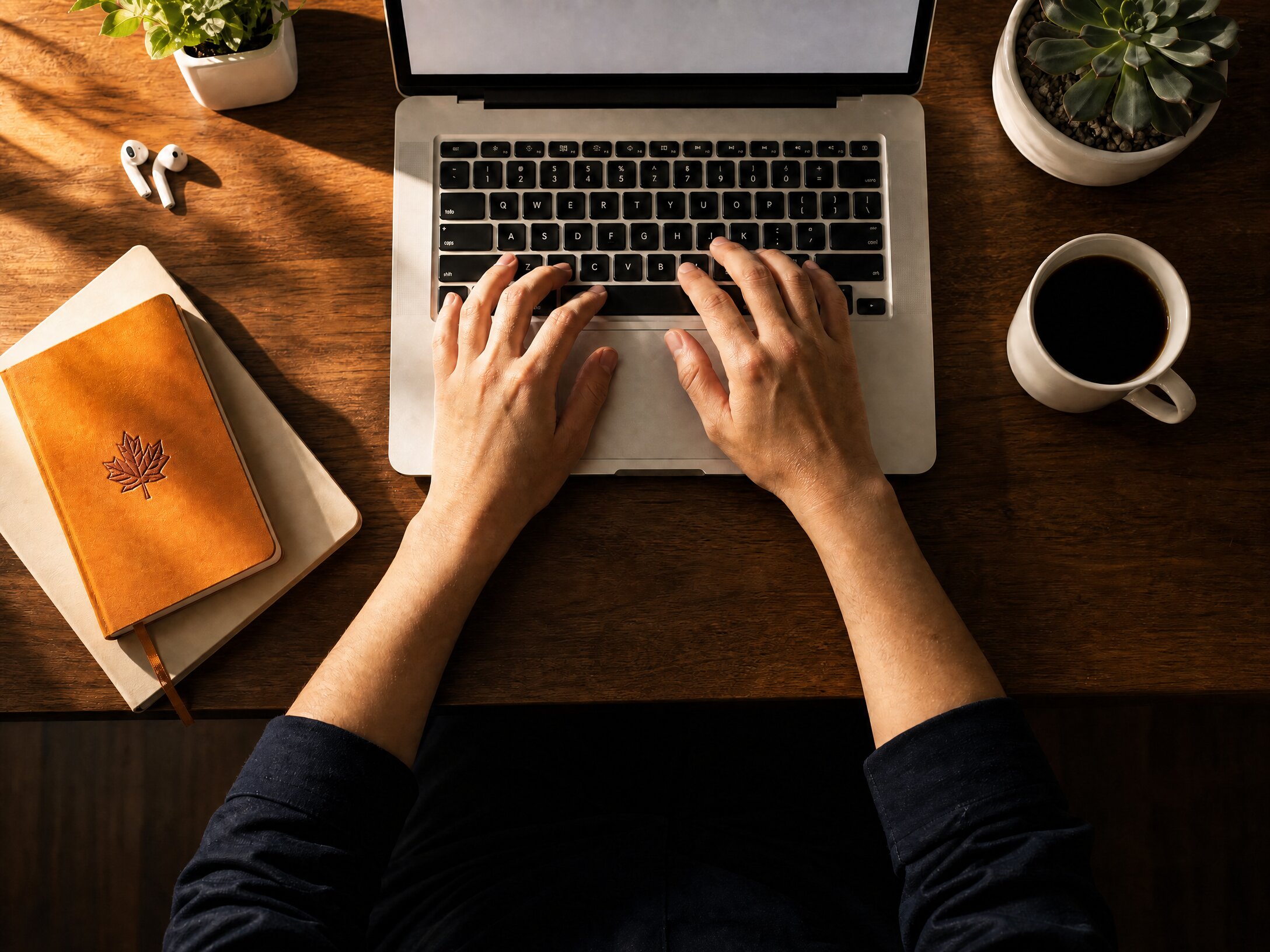 Someone reviewing their immigration plan on a laptop, notepad and coffee on a warm wooden desk